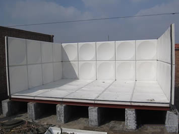 There is a white semi-manufactured SMC water tank on stone support frame.